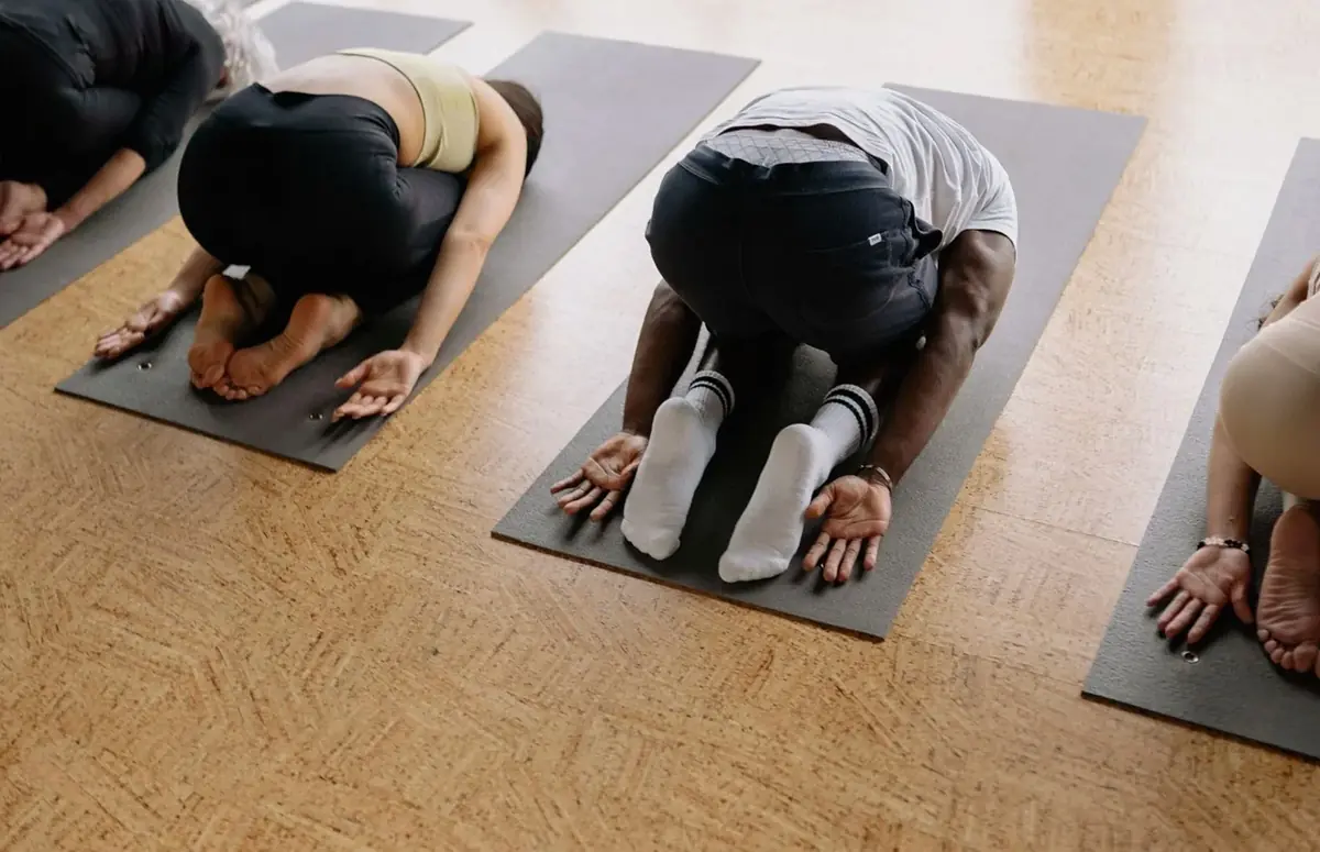 People in child's pose on yoga mats on a wooden floor