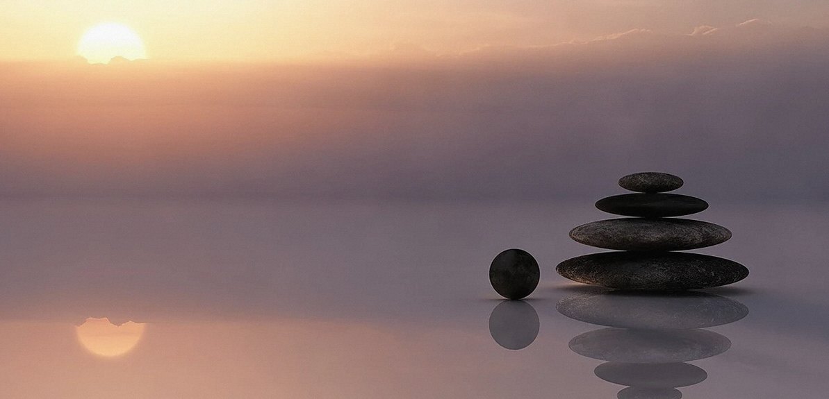 Stack of smooth dark stones balanced on calm water at sunrise