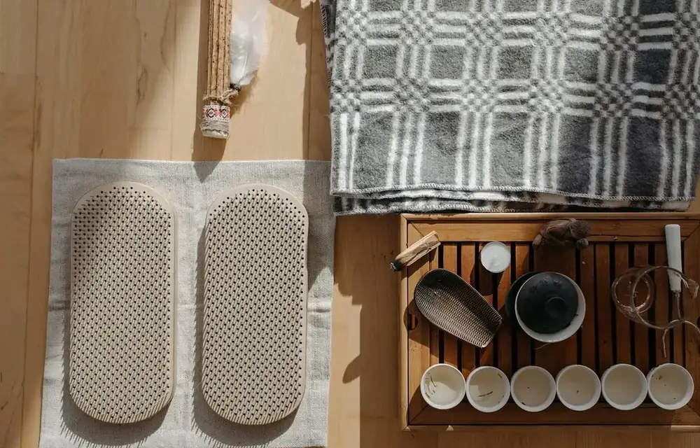 Overhead view of two beige pads, a woven blanket and a tea set on a wooden surface